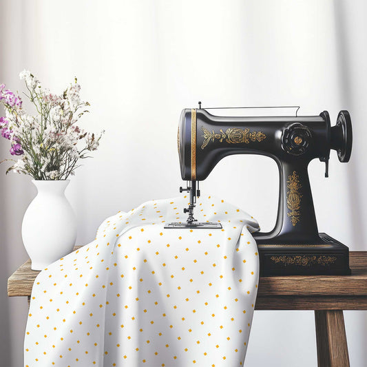 White Spun Polyester Fabric with Yellow-Orange Diamonds, FASP-1310-101, on an antique sewing machine sitting on a desk with vase of beautiful flowers.